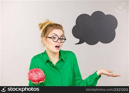 Business woman wearing green jacket and eyeglasses having doubt solution holding fake brain, black thinking or speech bubble next to her.. Business woman intensive thinking holding brain