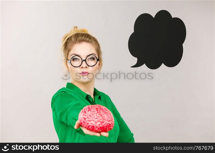 Business woman wearing green jacket and eyeglasses intensive thinking finding great problem solution holding fake brain, black thinking or speech bubble next to her.. Business woman intensive thinking holding brain