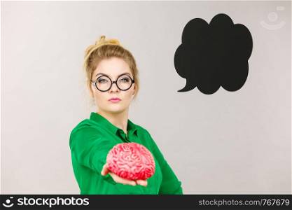 Business woman wearing green jacket and eyeglasses intensive thinking finding great problem solution holding fake brain, black thinking or speech bubble next to her.. Business woman intensive thinking holding brain