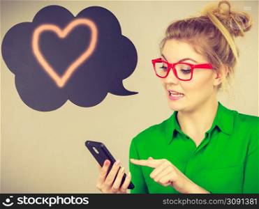 Business woman wearing green shirt and red eyeglasses looking at phone with black thinking or speech bubble next to her with heart sign. Business woman looking at phone, thinking bubble