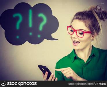 Business woman wearing green shirt and red eyeglasses looking at phone with black thinking or speech bubble next to her with ?!? text. Business woman looking at phone, thinking bubble