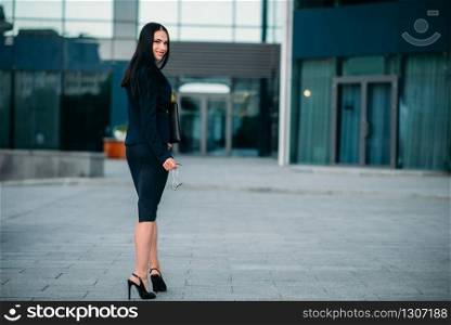Business woman with eyeglasses and laptop in hands, back view. Modern building, financial center, cityscape. Successful female businessperson. Business woman with laptop in hands, back view