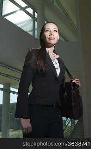 Business woman with handbag standing in office building, low angle view