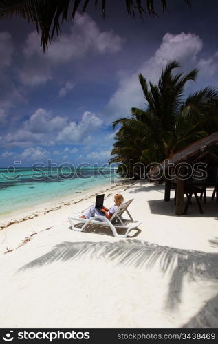 business woman with laptop lying on a chaise lounge in the tropical ocean coast