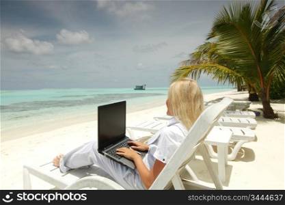 business woman with laptop lying on a chaise lounge in the tropical ocean coast