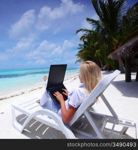 business woman with laptop lying on a chaise lounge in the tropical ocean coast