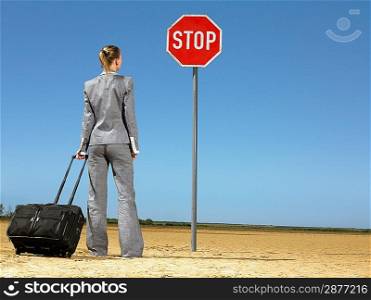 Business woman with luggage standing in front of stop sign in desert back view