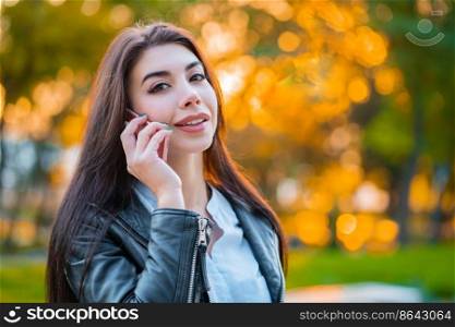 Business woman with smartphone close up in autumn park in sunset light. Girl have conversation with cell phone. Beautiful caucasian young woman talking with mobile device.. Business woman with smartphone close up in autumn park in sunset light. Girl have conversation with cell phone. Beautiful caucasian young woman talking with mobile device