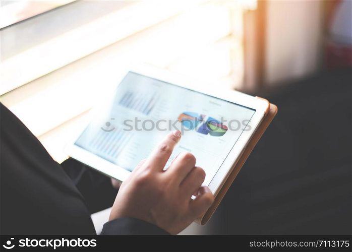 Business woman working in office with checking business report in a tablet / using a tablet computer for money analyzing graphs
