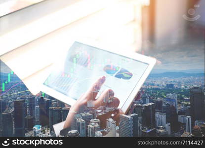 Business woman working in office with checking business report in a tablet / using a tablet computer for money analyzing graphs double exposure with city landscape and technology