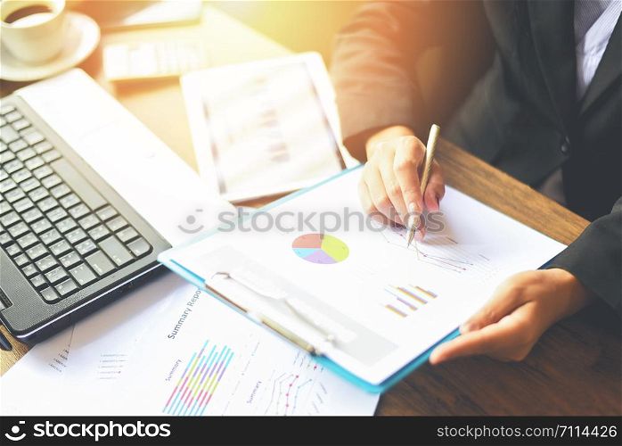 Business woman working in office with checking business report on the table desk with laptop tablet and coffee cup / Preparing report money analyzing graphs