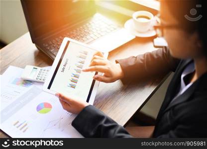 Business woman working in office with checking business report using tablet computer technology laptop with calculator and coffee cup / Sale report money analyzing graphs chart