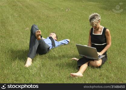 Business woman working in the grass while team mate takes a nap.