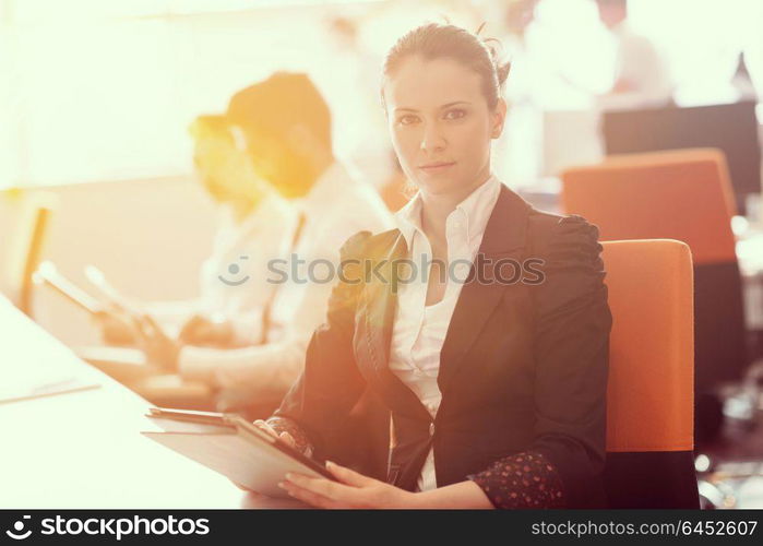 business woman working on desktop computer at modern startup office, people group in background with sunrise or sunset and sun flare in background