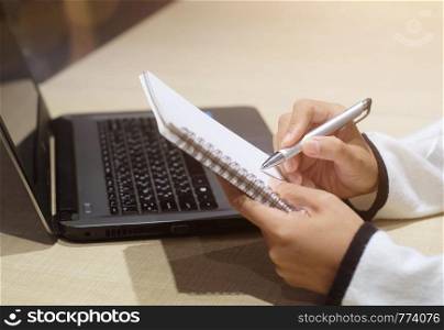 Business woman working on laptop and making note in a notebook. Online marketing, education, e-learning.