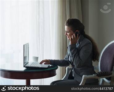 Business woman working on laptop and speaking mobile in hotel room