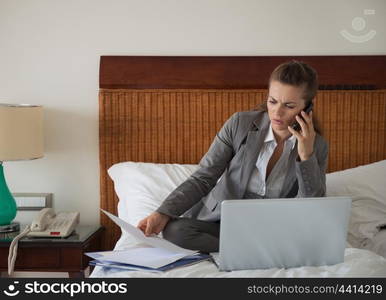 Business woman working with documents on bed in hotel room