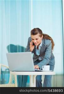 Business woman working with laptop and talking mobile phone on terrace