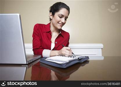 Business woman writing in diary beside laptop in office