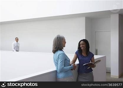 Business women standing, talking in office hallway