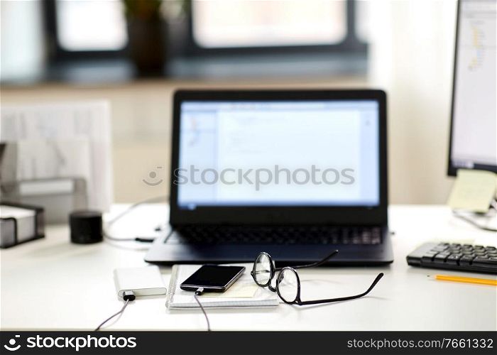 business, work and interior concept - laptop computer, smartphone, glasses and stationary on table at office. laptop, smartphone and notebook on table at office