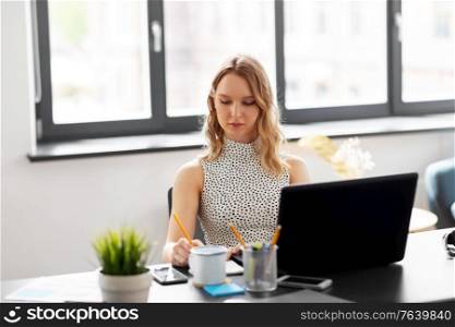 business, work and people concept - businesswoman sitting at table and writing to notebook at office. businesswoman writing to notebook at office