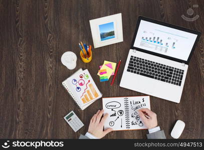 Business workplace with business stuff . Top view of business workplace and businessman hands writing in notepad