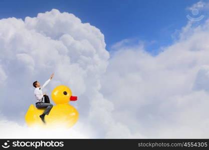 Businessman acting like child. Young happy businessman riding yellow rubber duck