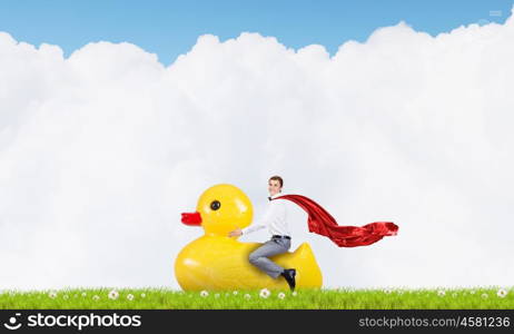 Businessman acting like child. Young happy businessman riding yellow rubber duck