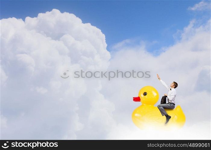Businessman acting like child. Young happy businessman riding yellow rubber duck