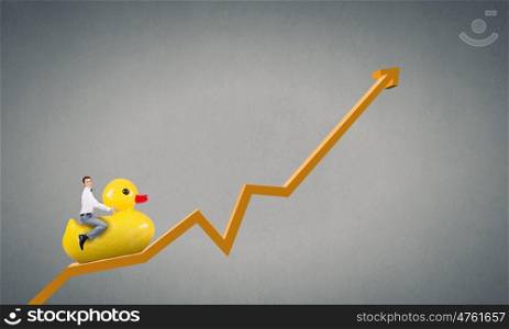 Businessman acting like child. Young happy businessman riding yellow rubber duck on growing graph