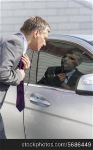 Businessman adjusting tie while looking in car window