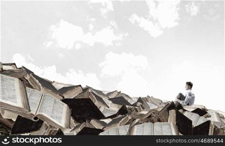 Businessman among old books. Young businessman sitting on pile of old books