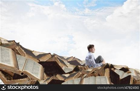 Businessman among old books. Young businessman sitting on pile of old books