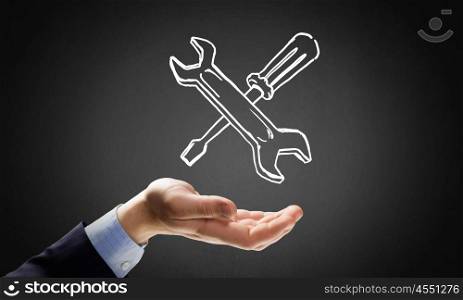 Businessman&amp;#39;s hand holding tools over gray background