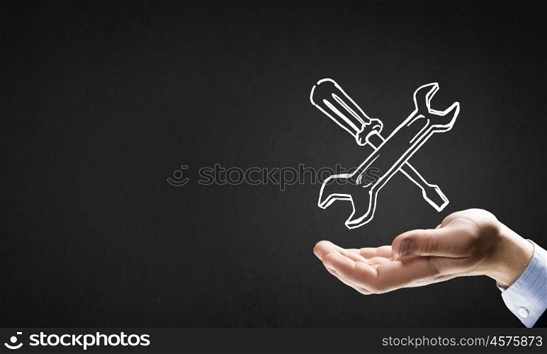 Businessman&amp;#39;s hand holding tools over gray background