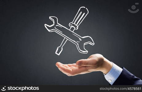 Businessman&amp;#39;s hand holding tools over gray background