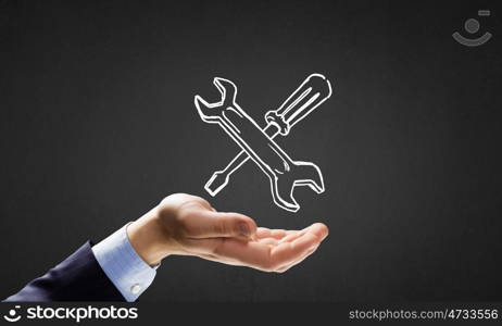 Businessman&amp;#39;s hand holding tools over gray background