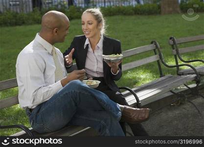 Businessman and a businesswoman having food on a park bench