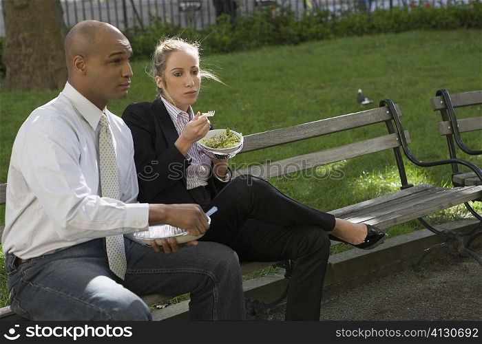 Businessman and a businesswoman having food on a park bench