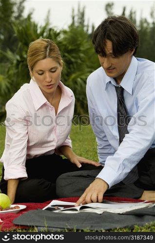 Businessman and a businesswoman reading a magazine in the park