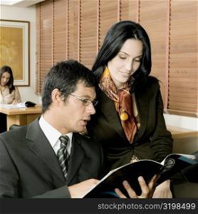 Businessman and a businesswoman sitting in an office and looking at a magazine