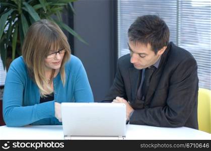 Businessman and a businesswoman sitting in front of a laptop