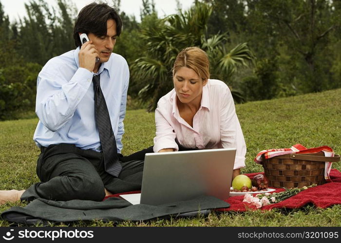 Businessman and a businesswoman sitting in front of a laptop in the park