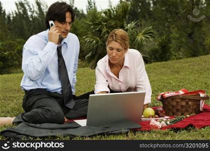 Businessman and a businesswoman sitting in front of a laptop in the park