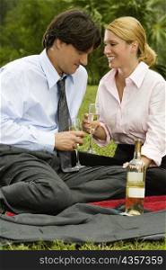 Businessman and a businesswoman sitting in the park holding champagne flutes