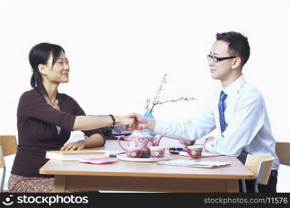 Businessman and a businesswoman sitting on chairs shaking hands