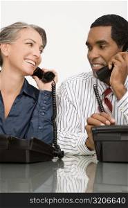 Businessman and a businesswoman talking on landline phones