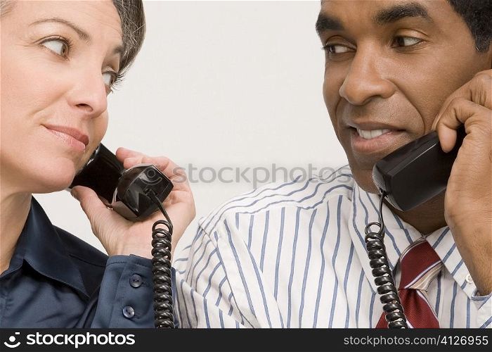 Businessman and a businesswoman talking on landline phones