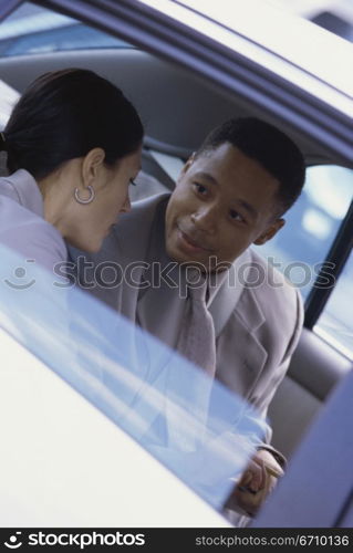 Businessman and a businesswoman talking to each other in the back seat of car